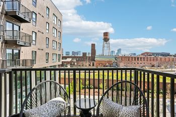 Two chairs with leopard print cushions are on a balcony overlooking a cityscape.